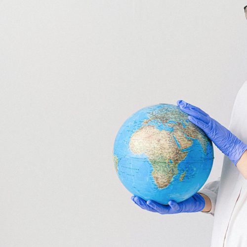 Person in mask and gloves holding a globe, symbolizing global healthcare during pandemic.